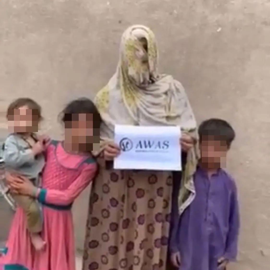 Une bénéficiaire de l'aide d'AWAS en Afghanistan prend la pose avec ses enfants et le logo de l'association. ©AWAS