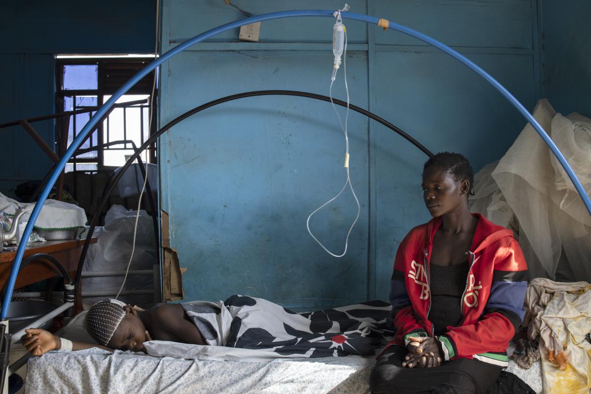 A 14-year-old boy rests at the hospital watched by his aunt after an attack on his village. © UNHCR/Hélène Caux